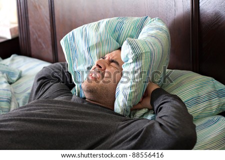 A man having trouble sleeping squeezes a pillow around his ears for some peace and quiet.