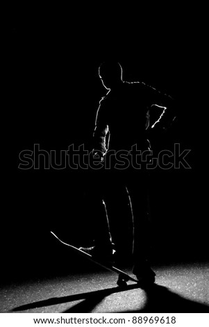 A rim lit skateboarder guy posing under dramatic back lighting with his skateboard flipped up in the front.