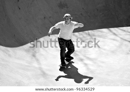 Black and white of a young skateboarder skating in the bottom of the bowl at a concrete skate park.