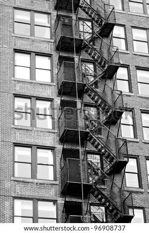 Exterior fire escape stairs on the outside of an old brick building in black and white.