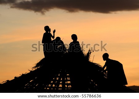 Masai Children thatching the roof of a traditional Masai hut at sunset. Taken at Oldukai, North Tanzania.