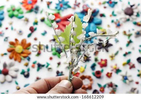 hand holds a silk flower over a plasticine colorful flowers background