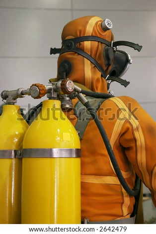 The diver is dressed in an orange diving suit, a rubber mask and on straps yellow oxygen cylinders hang