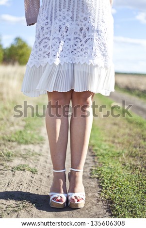 Portrait of barefoot woman in white dress walking on the road in the green field in summer