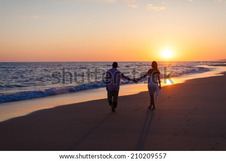 A silhouette of a happy family of two people, father and pregnant mother, are celebrating and praising God outside at sunset.