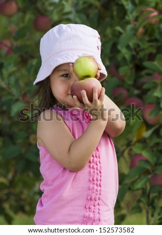 Child posing with 2 apples stacked above each other.