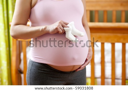 Pregnant woman holding baby socks. Crib is in background