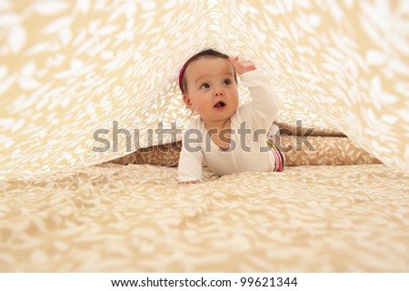 Baby girl under bed sheet and on her stomach.