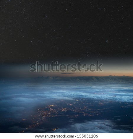 High altitude view of the Earth at night. City lights below the clouds, stars above.
