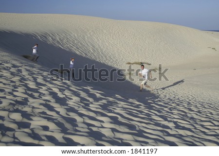 Three men running on a sand dune