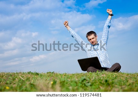 Young man with laptop Sits and Celebrates Outdoors