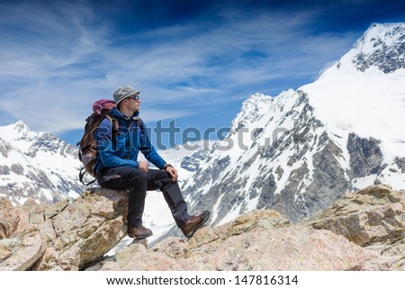 Young man with backpack sitting on cliff and looking at view