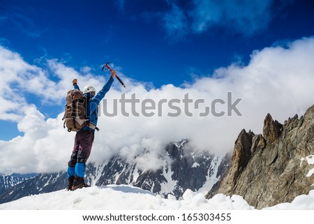 Winner / Success concept. Hiker cheering elated and blissful with arm raised in the sky after hiking to mountain top summit above the clouds