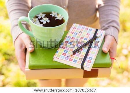 Closeup staked books in female hands, pencil and cup of spring tea. Spring inspiration ans reading concept background
