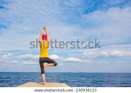 Young woman doing yoga pose under beautiful cloudy sky