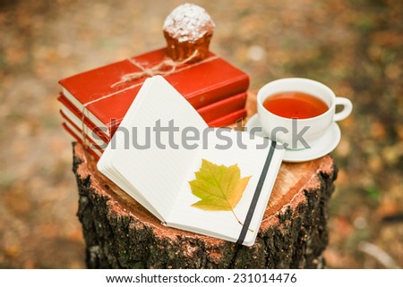 Cup of tea, stack of books with autumn leave on wooden background