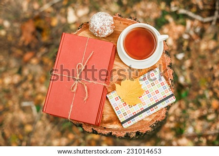 Cup of tea, stack of books with autumn leave on wooden background