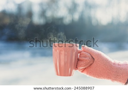 Female hands in mittens holding cup with hot tea or coffee. Winter and Christmas time concept