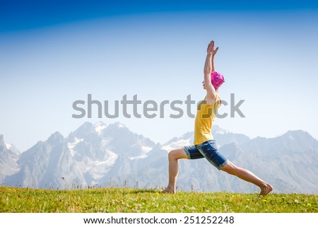 Young woman in warrior yoga pose standing on the grass under beautiful sky