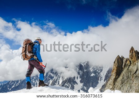 Mountaineer with ice ax reaches the top of a snowy mountain in a sunny winter day