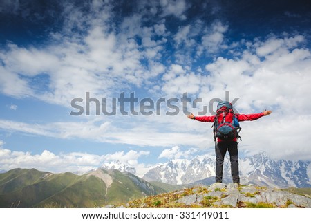 Happy hiker winning reaching life goal, success man at summit. Young hiker holding arms outstretched, freedom and happiness, achievement in mountains