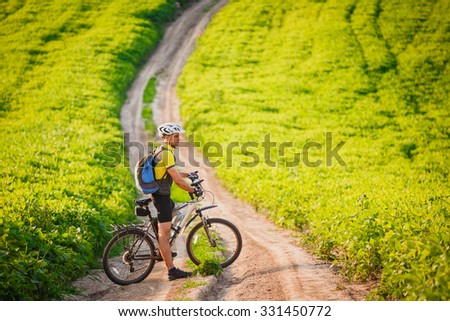 young athletic man on a bicycle rides on the green meadow road