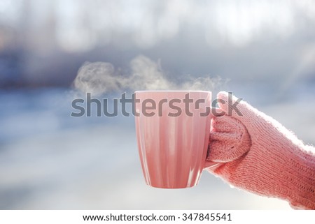Female hand in mittens holding cup with hot tea or coffee. Tea break. Winter and Christmas time concept