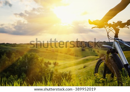 Lady with bicycle on a rural road with grass enjoying sunset