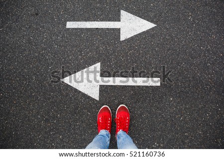Red sneakers on the asphalt road with drawn arrows pointing to two directions. Making decisions and making choices