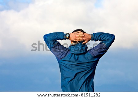 Young men with hands clasped behind a head look into the distance and have a rest at the sea coast