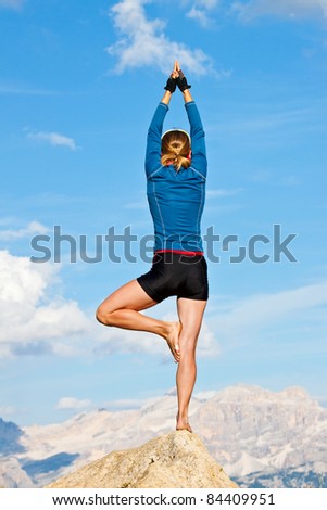 An attractive young woman doing a yoga pose for balance and stretching high in the mountains