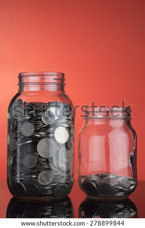 Saving Concept: Coins in two different level money jar on red background