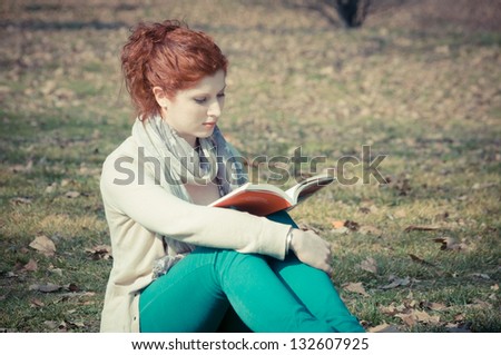 red long hair girl at the park reading in spring