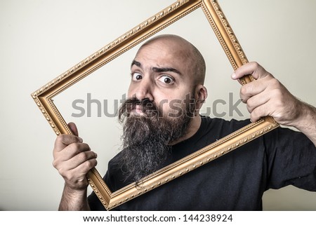 funny bearded man with golden frame on gray background