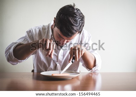 young stylish man with white shirt eating carrot behind a table