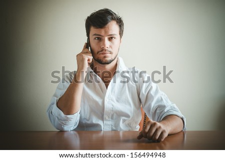 young stylish man with white shirt on the phone behind a table