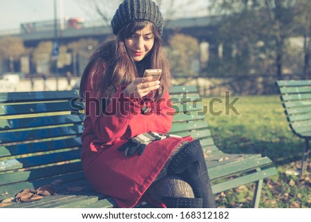 beautiful woman red coat winter bench park cellphone