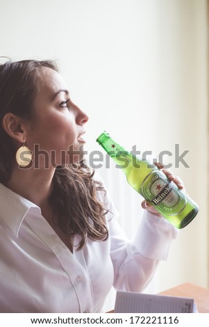 MILAN, ITALY - JANUARY 16, 2014: Woman drinking heineken beer glass bottle 33 cl. Heineken International is a Dutch brewing company, founded in 1864 in Amsterdam, famous all over the world.