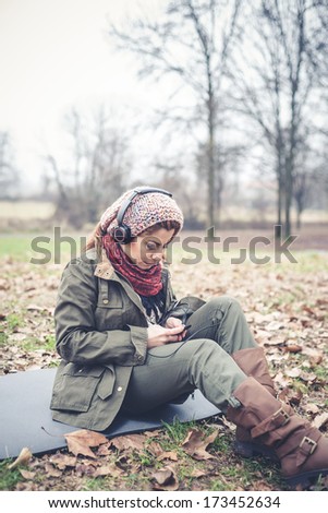 beautiful brunette woman listening to music with headphones at the park outdoor in winter