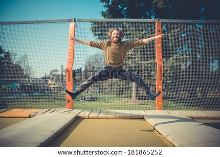 young bearded stylish handsome hipster man jumping on trampoline at playground