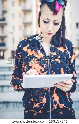 young beautiful punk dark girl using tablet in urban landscape