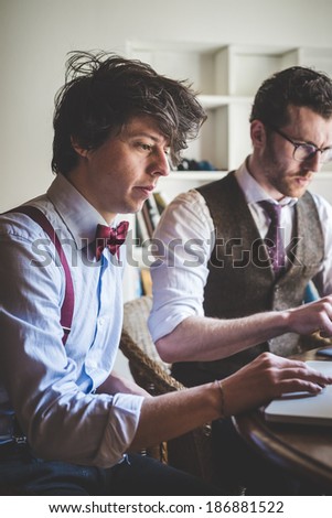 two young hipster stylish elegant men working with notebook and tablet at home