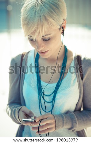 beautiful young blonde short hair hipster woman listening music earphones in the city