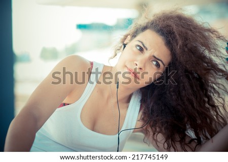 young beautiful long curly hair hipster woman listening to music with tablet in the city