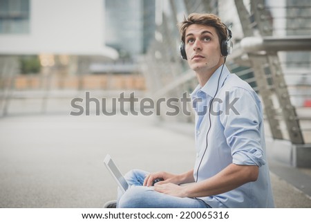 young model handsome blonde man with notebook and headphones in the city