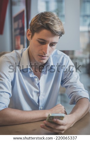 young model handsome blonde man using smartphone at the bar