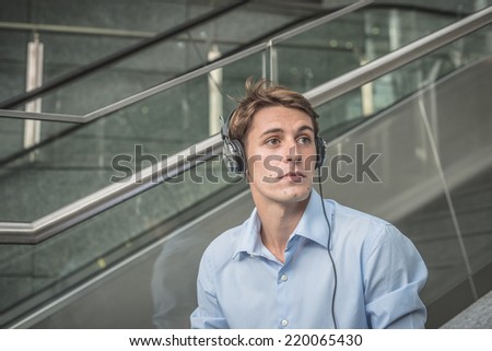 young model handsome blonde man with notebook smartphone and headphones in the city