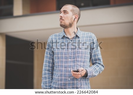 handsome hipster casual multitasking modern man listening music and using smartphone in the city
