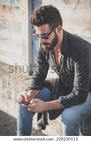 young handsome attractive bearded model man using smartphone in urban context