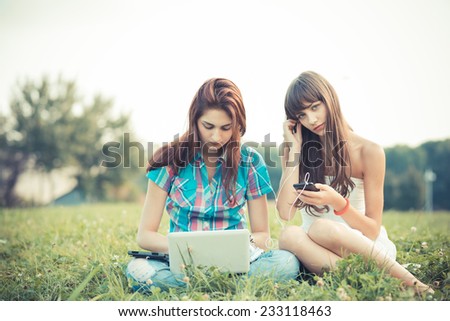beautiful hipster young women sisters friends using tablet and smartphone in the park